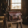 Longhorn full-grain leather saddle satchel with brass buckles on a wooden saddle stand in a Texas barn